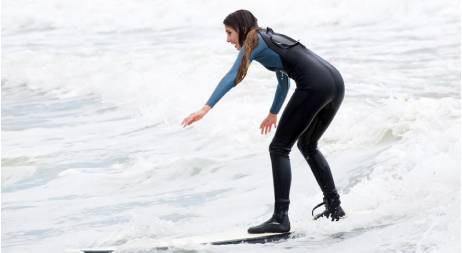 People in wetsuits ride yellow surfboards in shallow waves, and a person in a wetsuit surfboards on a white wave.
